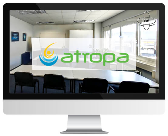 Auf einem Monitor ist ein heller Konferenzraum mit langem Tisch, Stühlen und dem „Atropa“-Logo zu sehen.